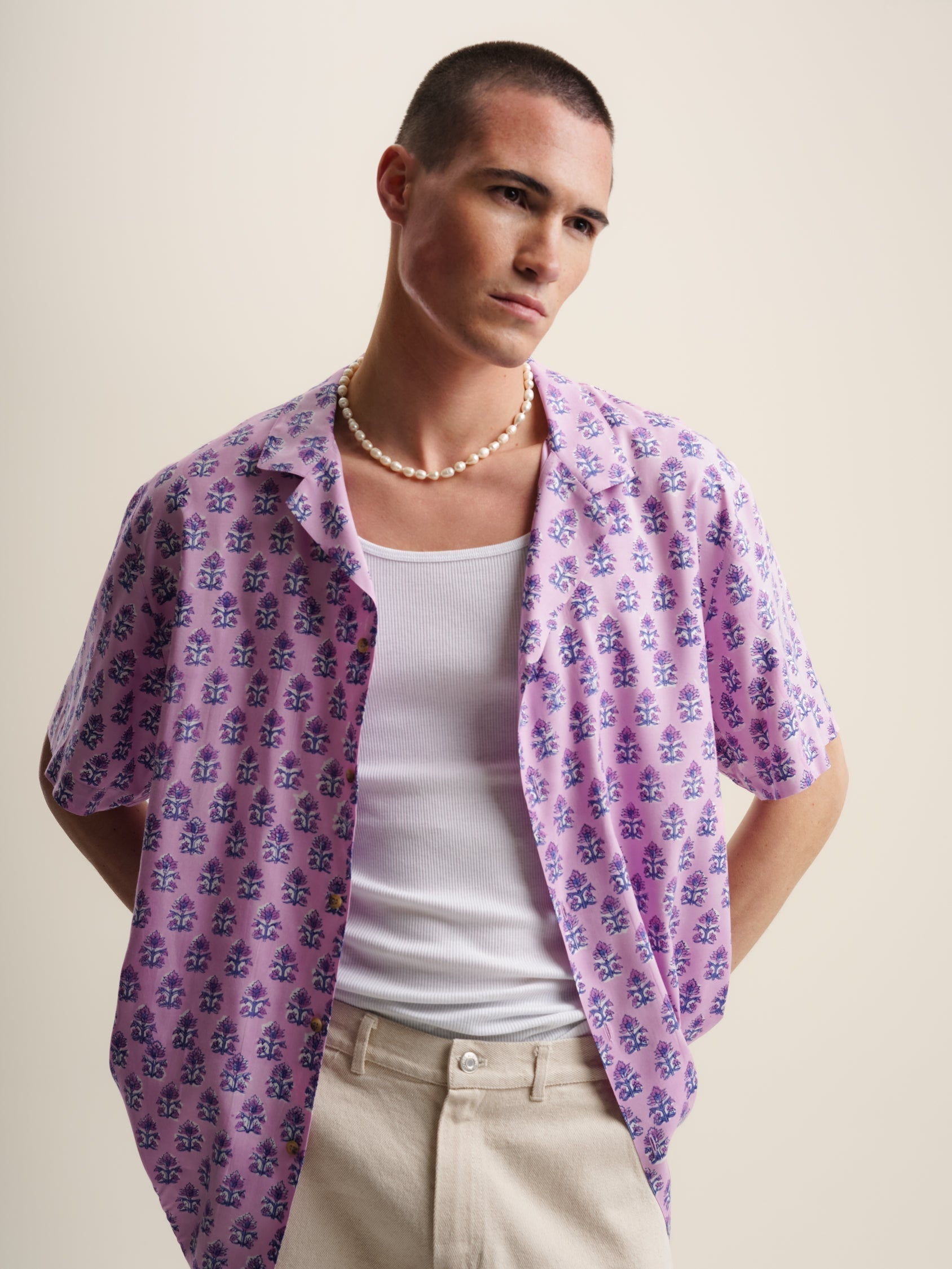 A stylish man wearing a pink lilac floral shirt and white pants.